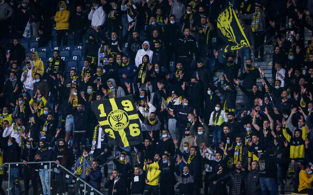 Soccer fans cheer during a match between Beitar Jerusalem FC and Ashdod FC at Teddy Kollek stadium in Jerusalem, on March 17, 2021. (Flash90) Soccer fans cheer during a match between Beitar Jerusalem FC and Ashdod FC at Teddy Kollek stadium in Jerusalem, on March 17, 2021. (Flash90)