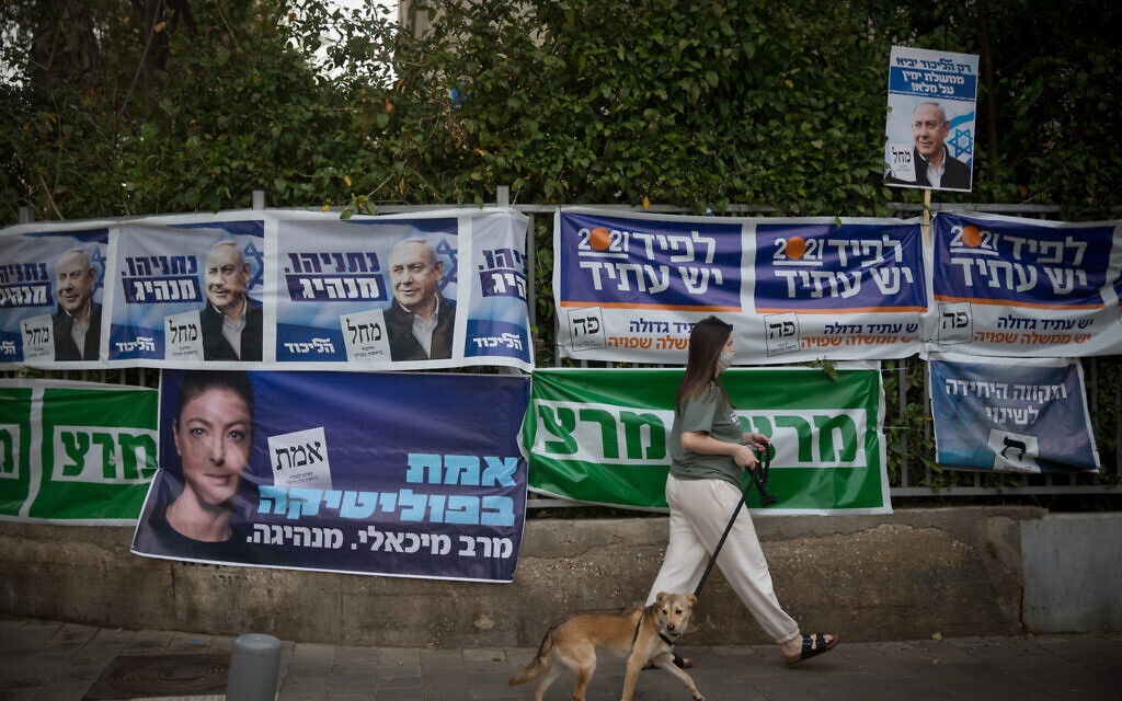 A woman walks past campaign posters in Tel Aviv on March 23, 2021. (Miriam Alster/Flash90)