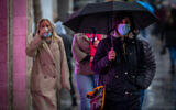 People wearing face masks take cover from rain as they walk on Jaffa Street in the city center of Jerusalem, on March 4, 2021. (Olivier Fitoussi/Flash90)