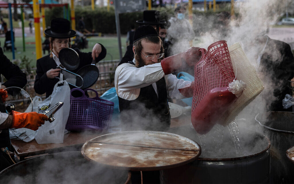 An ultra-Orthodox man dips cooking utensils in boiling water to remove remains of leaven in preparation for the upcoming holiday of Passover in Ashdod, March 25, 2021. (AP Photo/Tsafrir Abayov)