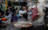 An ultra-Orthodox man dips cooking utensils in boiling water to remove remains of leaven in preparation for the upcoming holiday of Passover in Ashdod, March 25, 2021. (AP Photo/Tsafrir Abayov)