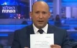 Naftali Bennett holds up a signed pledge not to serve in a government under Yair Lapid, on March 21, 2021 (Screen grab/Channel 20)