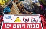 A sign that reads, "Danger, polluted sea" is placed on Haifa beach, northern Israel, next to bags full of tar collected by volunteers following an oil spill in the Mediterranean Sea, February 28, 2021. (AP Photo/Ariel Schalit)