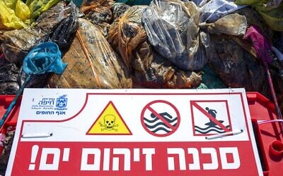 A sign that reads, "Danger, polluted sea" is placed on Haifa beach, northern Israel, next to bags full of tar collected by volunteers following an oil spill in the Mediterranean Sea, February 28, 2021. (AP Photo/Ariel Schalit)