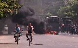 Cyclists pass police standing next to a burning makeshift tyre barricade, erected by protesters demonstrating against the military coup, in Yangon's South Okkalapa township on April 1, 2021. (STR / AFP)