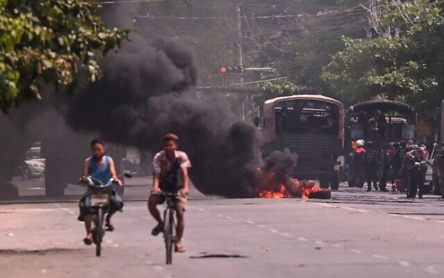 Cyclists pass police standing next to a burning makeshift tyre barricade, erected by protesters demonstrating against the military coup, in Yangon's South Okkalapa township on April 1, 2021. (STR / AFP) Cyclists pass police standing next to a burning makeshift tyre barricade, erected by protesters demonstrating against the military coup, in Yangon's South Okkalapa township on April 1, 2021. (STR / AFP)