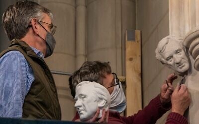 In this undated photo, sculptor Chas Fagan, left, holds a clay model of a bust of Elie Wiesel and watches as stonemason Sean Callahan, right, uses medieval techniques to carve the bust into the walls of the National Cathedral in Washington DC. (National Cathedral/ via JTA)