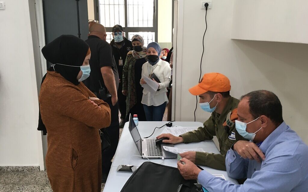 Roi Wolf, at computer, a sergeant in the Israeli army, processes would-be vaccination recipients while Kaisar Kabha, director of the Basma regional council, checks their identity documents. (Uriel Heilman/ JTA)