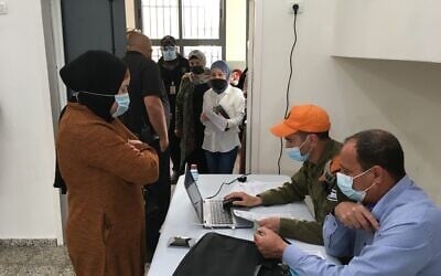 Roi Wolf, at computer, a sergeant in the Israeli army, processes would-be vaccination recipients while Kaisar Kabha, director of the Basma regional council, checks their identity documents. (Uriel Heilman/ JTA)