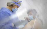 A man seen through plastic sheets gets a bandaid applied on his arm by a member of the medical staff after getting an AstraZeneca vaccine at a vaccination center in Bucharest, Romania, Wednesday, April 7, 2021.(AP Photo/Vadim Ghirda)