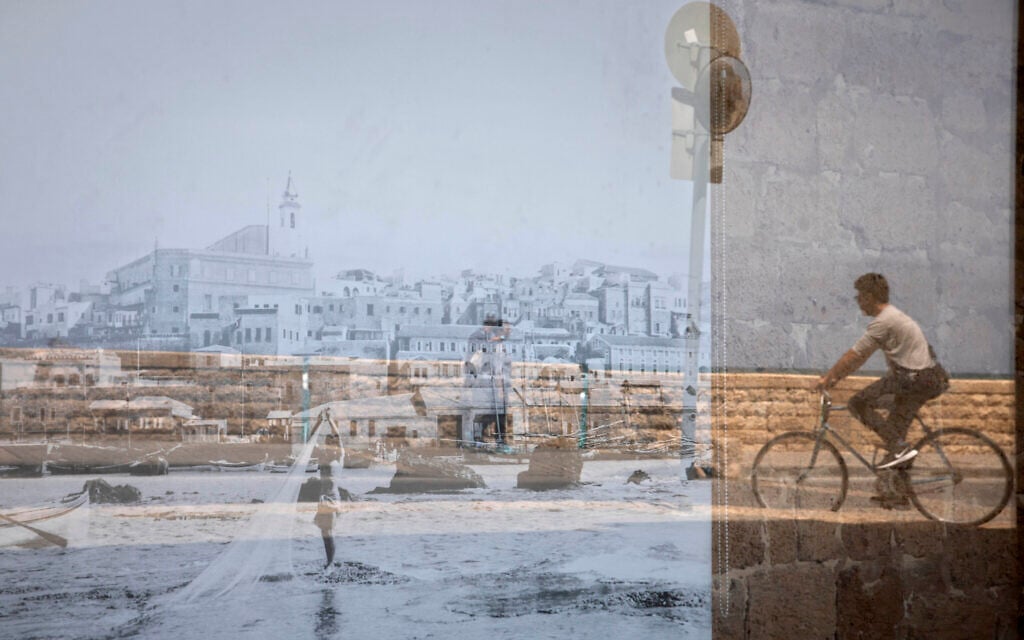A man riding his bicycle is reflected on an old picture of Jaffa displayed in a window, in the Jaffa neighborhood of Tel Aviv, Israel, April 21, 2021. (AP Photo/Sebastian Scheiner)