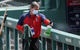 A Boston Red Sox staff member disinfects the railing in front of the visitor's dugout before a spring training baseball game between the Atlanta Braves and Boston Red Sox, March 10, 2021, in Fort Myers, Florida. (AP/John Bazemore)