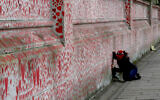 People paint red hearts marking the completion of the approximately 150,000 hearts being painted onto the National Covid Memorial Wall to commemorate all those who have died of coronavirus, on the Thames Embankment opposite the Houses of Parliament in London, April 8, 2021. (Frank Augstein/AP)