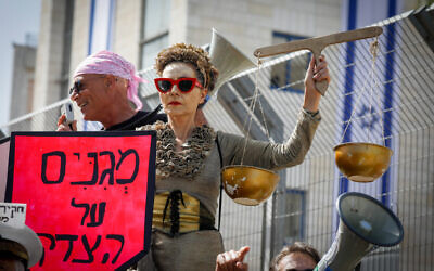 A protester holds symbolic scales of justice outside the District Court in Jerusalem, as Benjamin Netanyahu goes on trial on April 5, 2021. (Olivier Fitoussi/Flash90)