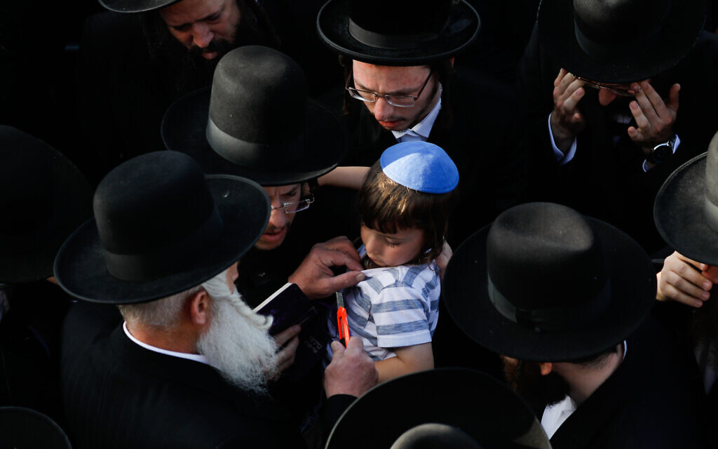 In a sign of mourning for one who lost a relative, a man cuts the shirt of the four-year-old son of Yehuda Leib Rubin who died in Meron tragedy, April 30, 2021 (Olivier Fitoussi/Flash90)