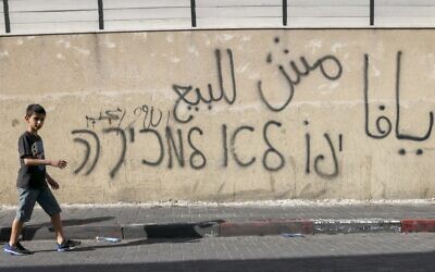 A boy walks past graffiti on a wall in Arabic and Hebrew which reads "Jaffa is not for sale" in the historic Arab neighborhood of Jaffa, south of Tel Aviv, on April 30, 2021. (AHMAD GHARABLI / AFP)