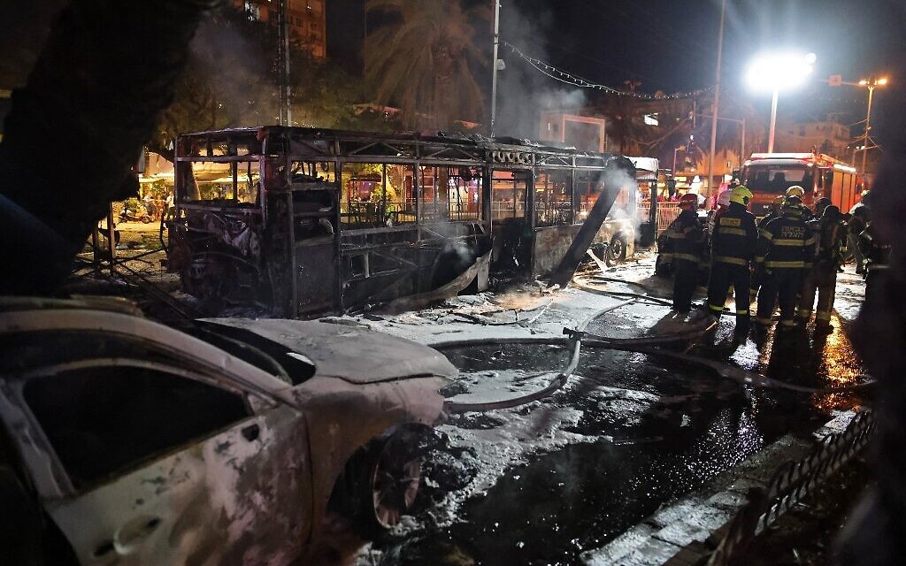 Israeli firefighters near a bus and other vehicles hit in a Gaza rocket strike on Holon near Tel Aviv, on May 11, 2021 (Ahmad Gharabli / AFP) Israeli firefighters near a bus and other vehicles hit in a Gaza rocket strike on Holon near Tel Aviv, on May 11, 2021 (Ahmad Gharabli / AFP)