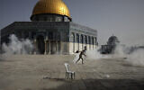 A Palestinian man runs away from tear gas during clashes with Israeli security forces in front of the Dome of the Rock Mosque at the Al Aqsa Mosque compound in Jerusalem's Old City, on May 10, 2021. (AP/Mahmoud Illean)