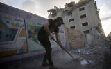 People clean the streets of debris beside a building that was previously damaged in an air-strike following a cease-fire reached after an 11-day war between Gaza's Hamas rulers and Israel, in Gaza City, May 21, 2021. (AP Photo/John Minchillo)