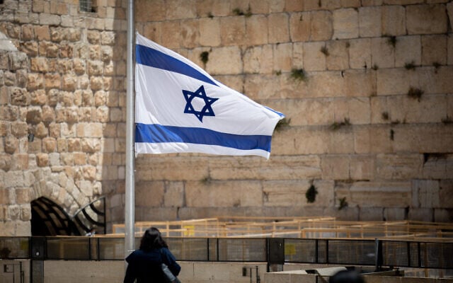 People walk next to an Israeli flag lowered to half-staff in honor of the Mt. Meron disaster victims, at the Western Wall in Jerusalem's Old City, May 2, 2021 (Yonatan Sindel/Flash90) People walk next to an Israeli flag lowered to half-staff in honor of the Mt. Meron disaster victims, at the Western Wall in Jerusalem's Old City, May 2, 2021 (Yonatan Sindel/Flash90)