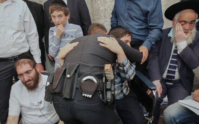 Police officer Rami Alwan hugs Shmuel Hayut, whom he saved at Meron. Father Avigdor Hayut sites to the left at their home in Bnei Brak, May 3, 2021 (Flash90) Police officer Rami Alwan hugs Shmuel Hayut, whom he saved at Meron. Father Avigdor Hayut sites to the left at their home in Bnei Brak, May 3, 2021 (Flash90)