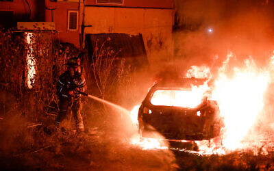 Firefighters put out a car of Jewish family that was set on fire in the East Jerusalem neighborhood of Sheikh Jarrah on May 6, 2021. (Olivier Fitoussi/Flash90)