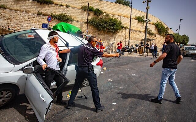 An Israeli policeman holds his weapon as he stands next to an injured Israeli man after his car crashed when a mob pelted his car with stones outside Jerusalem's Old City, May 10, 2021. (Olivier Fitoussi/Flash90) An Israeli policeman holds his weapon as he stands next to an injured Israeli man after his car crashed when a mob pelted his car with stones outside Jerusalem's Old City, May 10, 2021. (Olivier Fitoussi/Flash90)