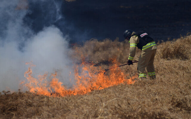 Israelis try to extinguish a fire caused from a rocket fired from the Gaza Strip near the Israeli-Gaza border, southern Israel, on May 16, 2021 (Tomer Neuberg/Flash90)