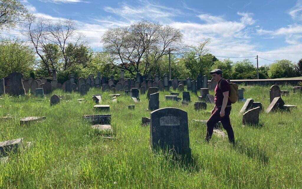 Matyas Kiraly walks among toppled and vandalized gravestones in the ancient Jewish cemetery in Nagyteteny, May 11, 2021. (Yaakov Schwartz/ Times of Israel)