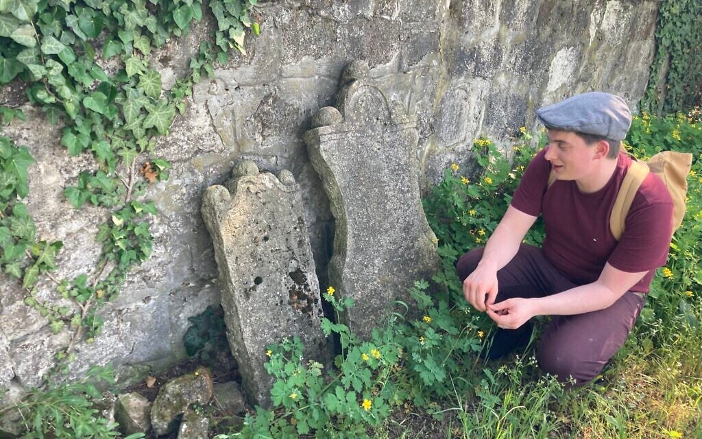 Matyas Kiraly kneels next to some of the oldest gravestones, dating back to 1750, in the ancient Jewish cemetery in Nagyteteny, May 11, 2021. (Yaakov Schwartz/ Times of Israel)
