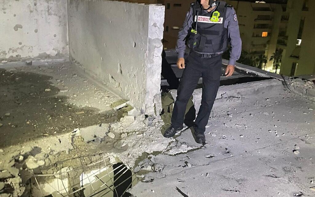 A firefighter stands over the impact site of a rocket fired from the Gaza Strip that hit a building in the city of Ashkelon, critically injuring a man, on May 14, 2021. (Fire and Rescue Services)