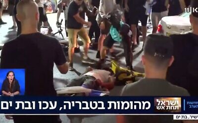 A man beats a man lying prone on the ground in Bat Yam, amid interethnic violence across Israel, May 12, 2021. (Kan TV Screenshot)