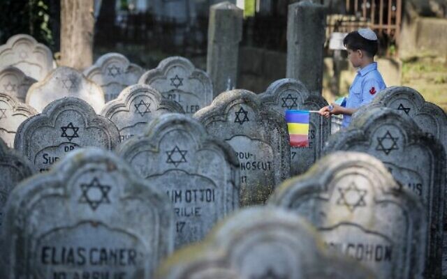 A child wearing a kippa and holding a Romanian flag walks past tombstones at the Jewish cemetery in the city of Iasi, Romania, on June 29, 2021. (Liviu Chirica/AFP) A child wearing a kippa and holding a Romanian flag walks past tombstones at the Jewish cemetery in the city of Iasi, Romania, on June 29, 2021. (Liviu Chirica/AFP)