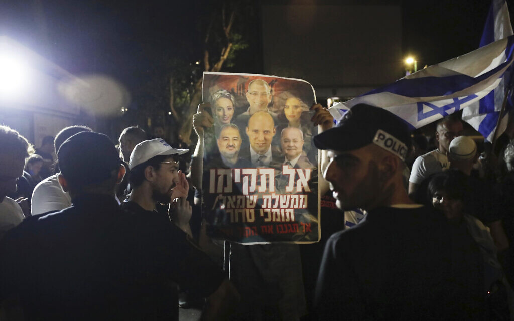 Israeli police officers stand guard as right-wing protesters chant slogans and hold signs showing Naftali Bennett and other members of the Yamina party with Arab politicians Ahmad Tibi, right, and Mansour Abbas, left, during a demonstration in the central Israeli city of Ramat Gan, June 2, 2021. The Hebrew sign reads, 'Don't form a left-wing government with supporters of terror.' (AP/Sebastian Scheiner)