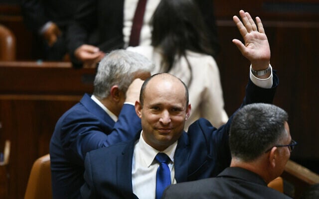 Newly elected Prime Minister Naftali Bennett waves, with Yair Lapid (left) and Gideon Sa'ar (right) alongside him, after their new coalition wins Knesset approval, June 13, 2021 (Haim Zach / GPO)