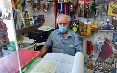 Shai Berlin behind a newly re-erected Perspex screen in his hardware store in Binyamina on June 21, 2021. (Nathan Jeffay/Times of Israel)