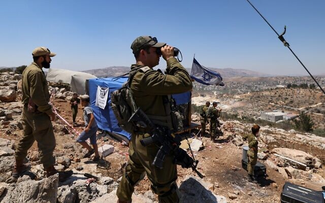 Illustrative: Israeli soldiers observe the Palestinian village of Beita with binoculars as settlers evacuate the newly-established wildcat outpost of Evyatar near the northern Palestinian city of Nablus in the West Bank, on July 2, 2021 (Emmanuel DUNAND / AFP)