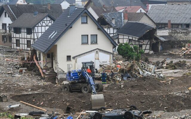 An excavator digs a hole next to a car that lies upside down after the floods caused major damage in Schuld near Bad Neuenahr-Ahrweiler, western Germany, on July 17, 2021. (Christof Stache/AFP)
