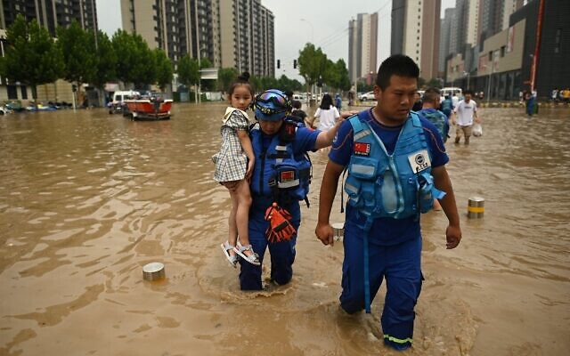 Members of rescue organization Bluesky rescue team carry a girl across a flooded street following a heavy rain in Zhengzhou, in China's Henan province, on July 22, 2021. (Noel Celis/AFP) Members of rescue organization Bluesky rescue team carry a girl across a flooded street following a heavy rain in Zhengzhou, in China's Henan province, on July 22, 2021. (Noel Celis/AFP)