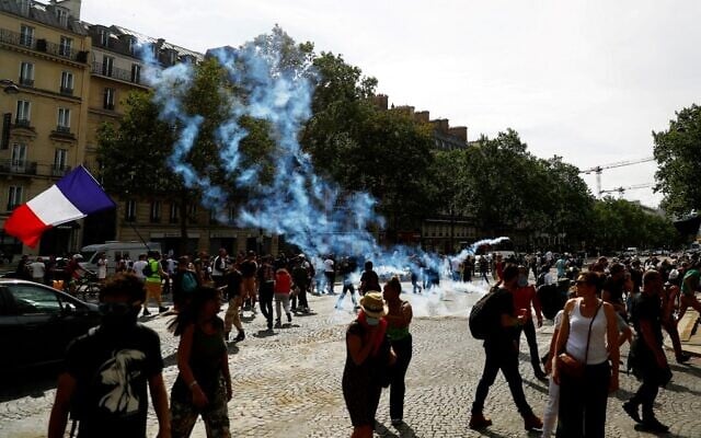 Prosters stand amidst tear gas smoke on the Champs Elysees avenue during clashes on the sidelines of a demonstration against the compulsory vaccination for certain workers and the mandatory use of the health pass called by the French government in Paris, on July 24, 2021. (Sameer Al-Doumy/AFP) Prosters stand amidst tear gas smoke on the Champs Elysees avenue during clashes on the sidelines of a demonstration against the compulsory vaccination for certain workers and the mandatory use of the health pass called by the French government in Paris, on July 24, 2021. (Sameer Al-Doumy/AFP)