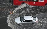A car and a bus drives through deep water on a flooded road in The Nine Elms district of London on July 25, 2021. (JUSTIN TALLIS / AFP)