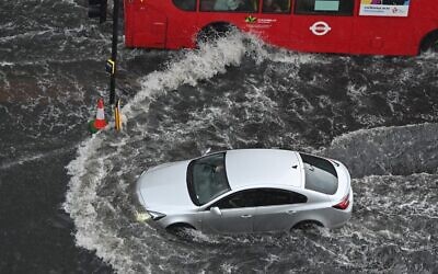 A car and a bus drives through deep water on a flooded road in The Nine Elms district of London on July 25, 2021. (JUSTIN TALLIS / AFP)