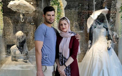 Illustrative: Newly married Iranian couple Mohammad Davoodi, 28, and his wife Mahsa Asadzadeh, 20, pose for a photo in front of a wedding dress shop in downtown Tehran, Iran, on July 3, 2019. (AP/Ebrahim Noroozi)