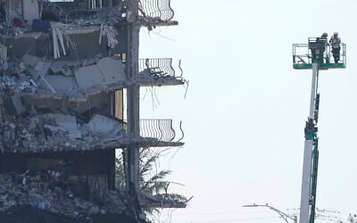 Workers stand watch from a lift beside the partially collapsed Champlain Towers South condo building, where demolition experts were preparing to bring down the precarious still-standing portion, Sunday, on July 4, 2021, in Surfside, Florida. (AP/Lynne Sladky)