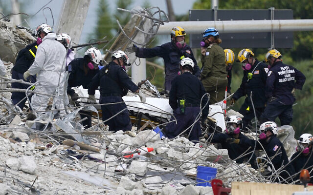 In this Monday, July 5, 2021, file photo, rescue workers move a stretcher containing recovered remains at the site of the collapsed Champlain Towers South condo building, in Surfside, Florida. (AP/Lynne Sladky) In this Monday, July 5, 2021, file photo, rescue workers move a stretcher containing recovered remains at the site of the collapsed Champlain Towers South condo building, in Surfside, Florida. (AP/Lynne Sladky)