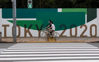Men cycle along the wall installed to close off a park being prepared for the Olympics and Paralympics Games in Tokyo on July 1, 2021. (AP Photo/Hiro Komae)