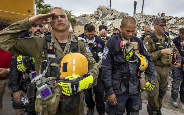 A member of the Israeli search and rescue team, left, salutes in front of the rubble that once was Champlain Towers South during a prayer ceremony, on July 7, 2021, in Surfside, Florida. (Jose A Iglesias/Miami Herald via AP)