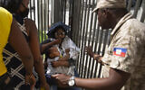 A Haitian police asks a woman to move away from a gate at the U.S. Embassy in Port-au-Prince, Haiti, July 9, 2021. A large crowd gathered outside the embassy amid rumors on radio and social media that the US will be handing out exile and humanitarian visas, two days after Haitian President Jovenel Moise was assassinated in his home. (AP Photo/Joseph Odelyn)