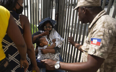 A Haitian police asks a woman to move away from a gate at the U.S. Embassy in Port-au-Prince, Haiti, July 9, 2021. A large crowd gathered outside the embassy amid rumors on radio and social media that the US will be handing out exile and humanitarian visas, two days after Haitian President Jovenel Moise was assassinated in his home. (AP Photo/Joseph Odelyn)