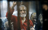 Muslim Brotherhood spiritual leader Mohammed Badie waves from a defendants cage in a makeshift courtroom at the national police academy, in eastern Cairo, Egypt, May 16, 2015. (Ahmed Omar/AP)